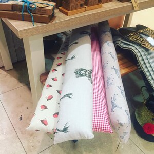May include: A display of decorative door draft stoppers. The stoppers feature various patterns, including red birds, green birds, zebras, and a red and white gingham check. The stoppers are cylindrical and made of fabric.