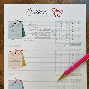 Peut inclure: Un suivi des cadeaux de Noël avec un nœud rouge en haut. Le suivi comprend des sections pour les idées cadeaux, le type, le prix et si le cadeau est acheté, fabriqué, emballé et prêt. Un stylo rose repose sur la page.