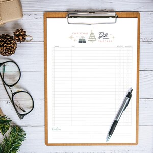 Peut inclure: Un presse-papiers en bois avec un suivi des cadeaux de Noël. Le haut de la page affiche "Christmas Gift Tracker" avec des illustrations festives. Un stylo est posé sur le côté droit. Fond en bois blanc.