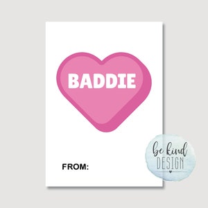 Puede incluir: Una tarjeta rosa en forma de coraz&oacute;n con la palabra "BADDIE" en texto blanco. La tarjeta tiene las palabras "FROM:" en la parte inferior.