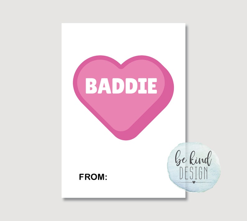 Puede incluir: Una tarjeta rosa en forma de coraz&oacute;n con la palabra "BADDIE" en texto blanco. La tarjeta tiene las palabras "FROM:" en la parte inferior.