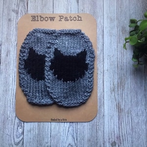 Könnte beinhalten: Zwei graue gestrickte Ellenbogen-Patches mit schwarzen Katzenpfotenabdrücken. Die Patches befinden sich auf einer braunen Karte mit dem Text "Elbow Patch" und "Sewed by a Kris".