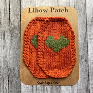 May include: Two orange knitted elbow patches with green heart designs. The patches are displayed on a brown card with the text "Elbow Patch" and "Sealed by a Kris".
