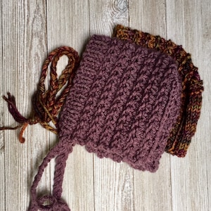 May include: A purple knitted baby bonnet with a long tie, and a multi-colored yarn skein.