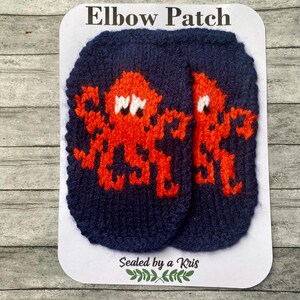 May include: Navy blue elbow patches with an orange octopus design and the text "Elbow Patch". The patches are on a white card with the text "Sealed by a Kris".
