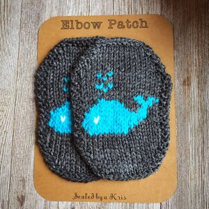 Puede incluir: Dos parches de codo de punto gris con un diseño de ballena azul y corazones blancos. Los parches están en una tarjeta marrón con el texto "Elbow Patch" y "Sealed by a Kris".