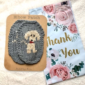 May include: Two gray knitted elbow patches with a white dog design. The patches are on a brown card with the text "Elbow Patch" and "Sealed by a Kris".