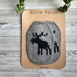 May include: Two gray knitted elbow patches with a black moose design. The patches are packaged on a brown card with the text "Elbow Patch" and "Sealed by a Kris".