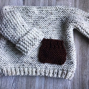 May include: A white knitted sweater with a brown knitted patch pocket.