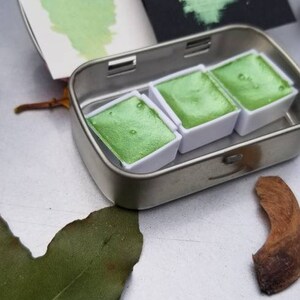 May include: A metal tin with three pans of green watercolor paint. The pans are labeled "Holly Green".