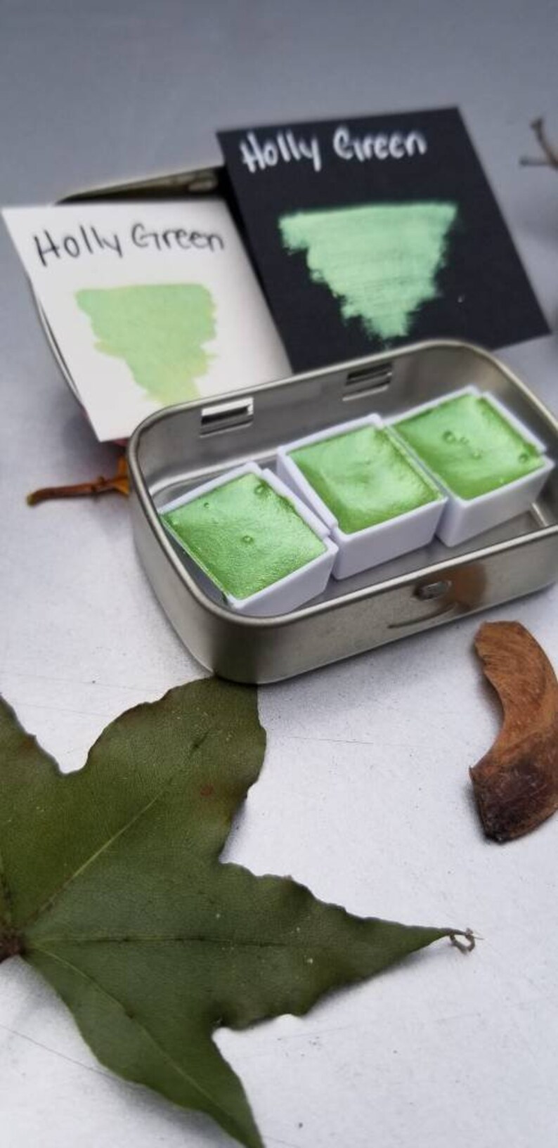 May include: A metal tin with three pans of green watercolor paint. The pans are labeled "Holly Green".