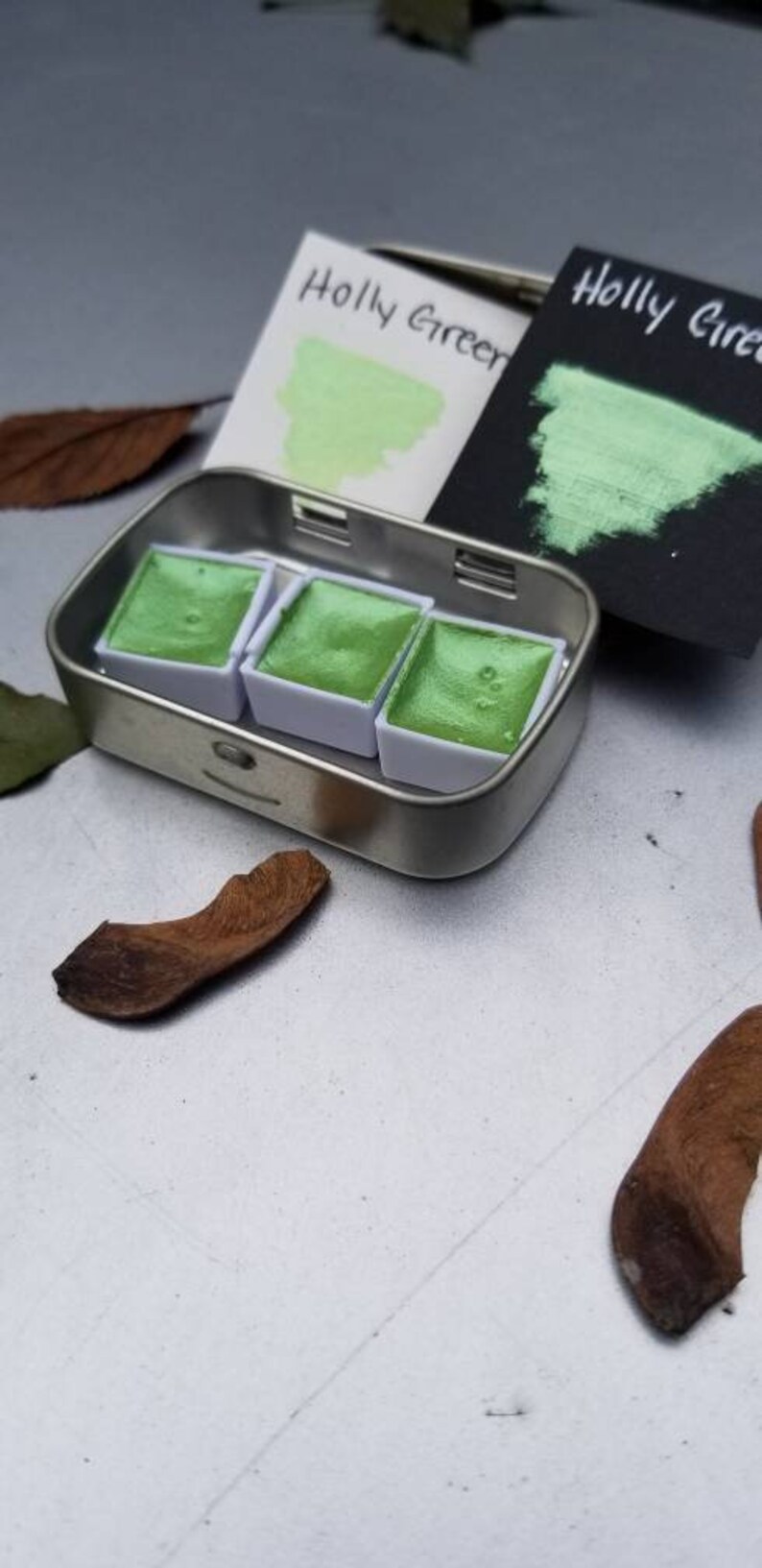 May include: A metal tin with three pans of green watercolor paint. The tin has a label that says "Holly Green".
