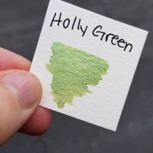 May include: A white card with the text "Holly Green" written in black ink. A green ink sample is on the card.