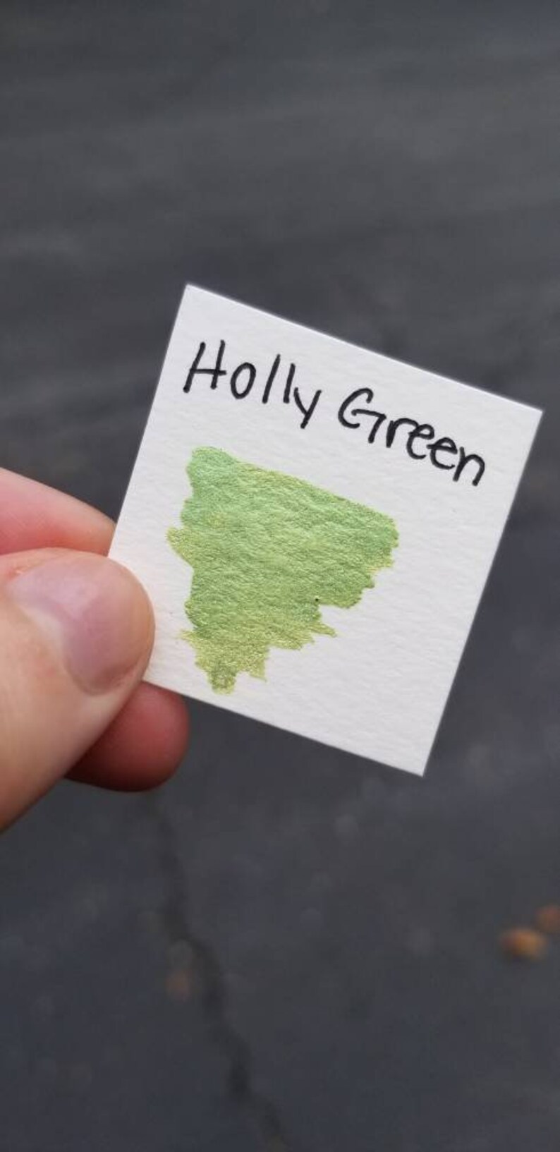 May include: A white card with the text "Holly Green" written in black ink. A green ink sample is on the card.