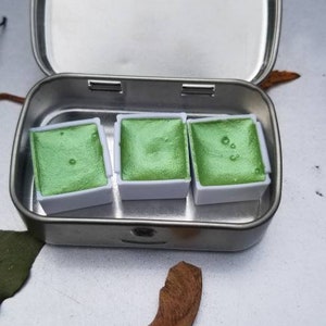 May include: A metal tin with three small pans of green watercolor paint.