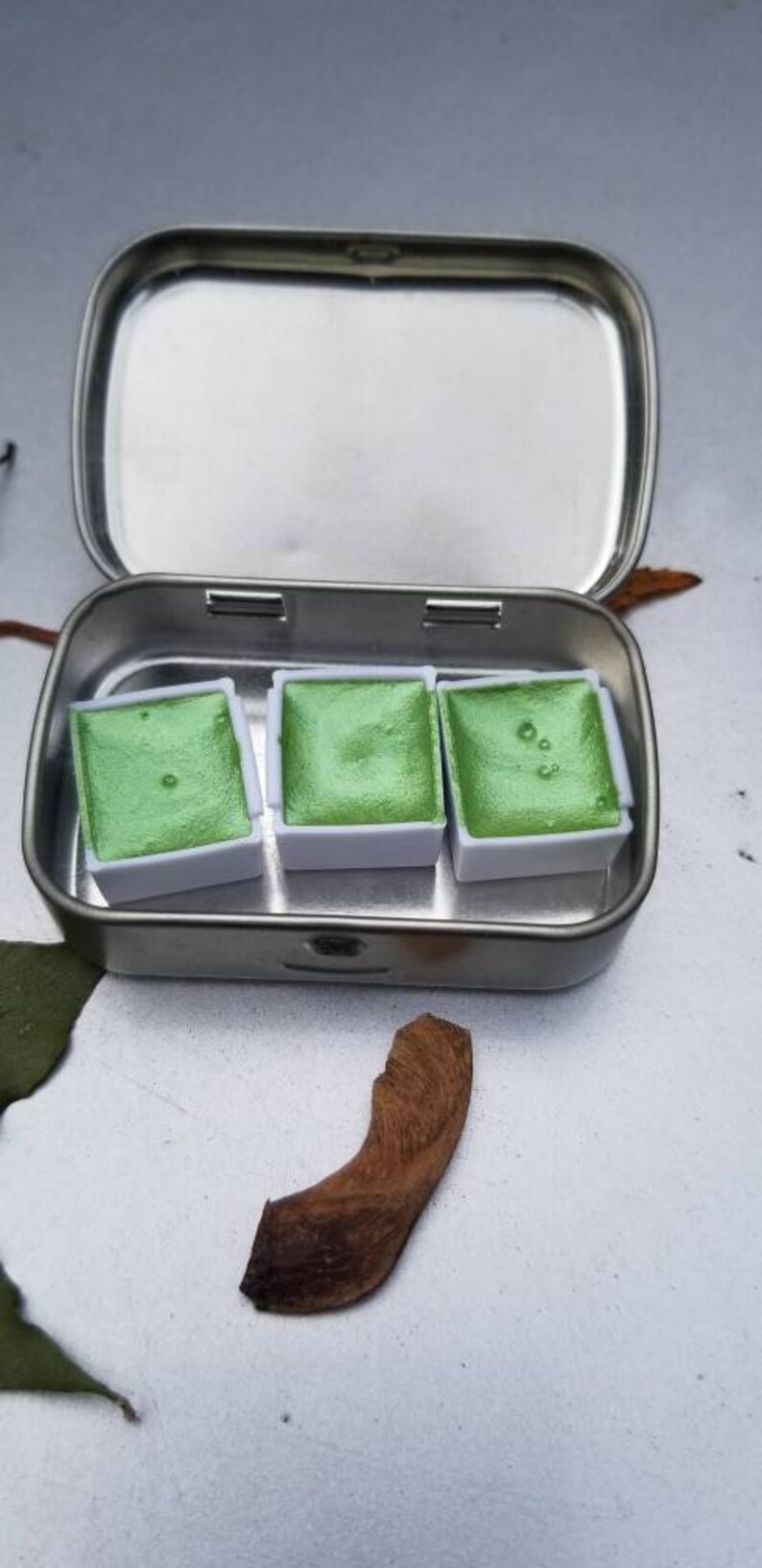 May include: A metal tin with three small pans of green watercolor paint.