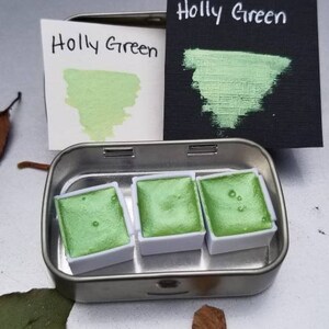 May include: A metal tin with three pans of green watercolor paint. The pans are labeled "Holly Green".