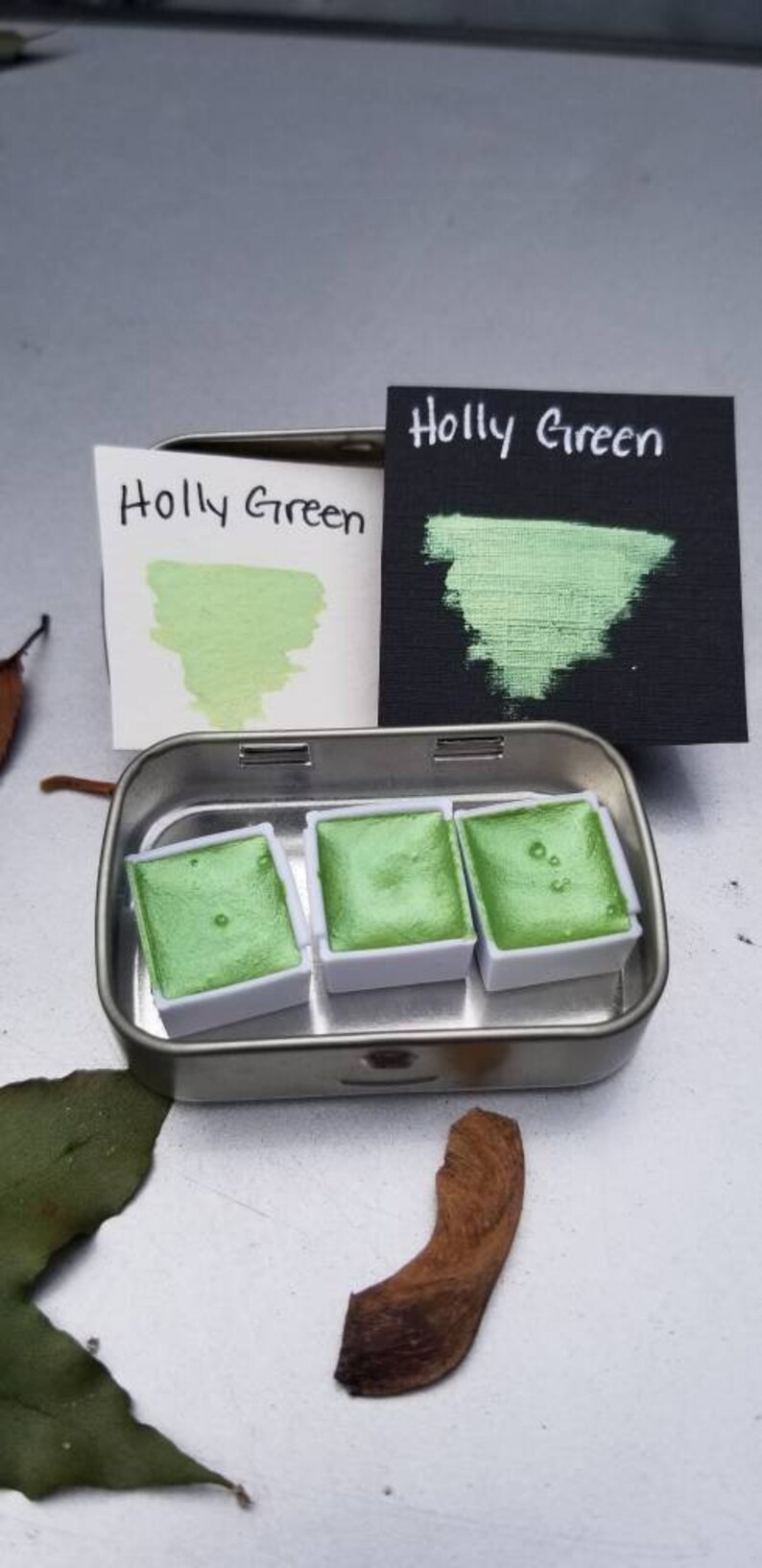 May include: A metal tin with three pans of green watercolor paint. The pans are labeled "Holly Green".