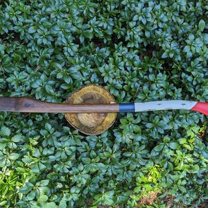May include: A wooden axe handle with a red, white and blue painted design. The handle is resting on a tree stump.