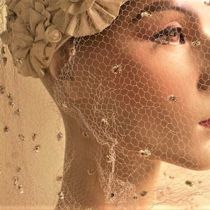 May include: A vintage-style bridal veil with a delicate net fabric and small, sparkling embellishments. The veil is worn over a mannequin's head, covering the face and hair.