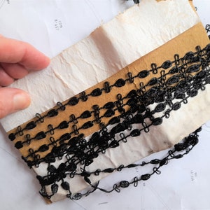 May include: Black trim with a delicate chain-like design. The trim is wrapped around a piece of cardboard.