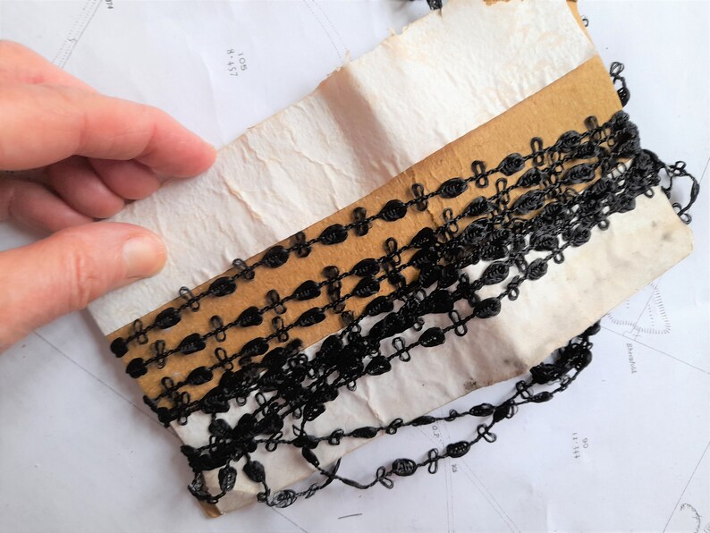 May include: Black trim with a delicate chain-like design. The trim is wrapped around a piece of cardboard.