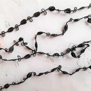 May include: Black trim with a delicate, knotted design. The trim is made of a thin, flexible material and has a subtle sheen.