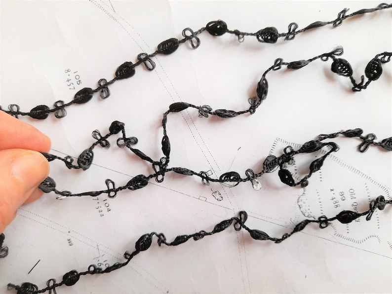 May include: Black trim with a delicate, knotted design. The trim is made of a thin, flexible material and has a subtle sheen.