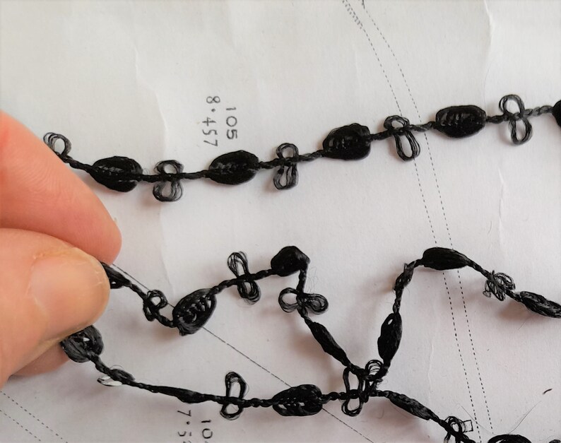May include: Black trim with a knotted design. The trim is made of a thin, flexible material and has a series of small, evenly spaced knots.