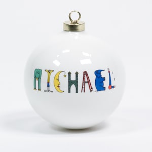 May include: White ceramic Christmas ornament with the name "MICHAEL" spelled out in colorful letters and illustrations. The letters are decorated with a green elephant, a man in a yellow jacket, a yellow crescent moon, a green castle, a red ladder, a red slide, and a blue elephant.