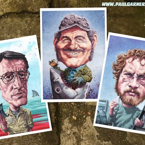 May include: Three cartoon illustrations of characters from the movie Jaws. The first illustration is of a man in a yellow shirt holding a book titled "Jaws". The second illustration is of a man in a green shirt holding a glass of beer and standing on a shark. The third illustration is of a man in a blue shirt holding a spear gun and a small creature.