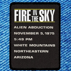 May include: A black rectangular patch with white text and a yellow border. The text reads "FIRE IN THE SKY" above the words "ALIEN ABDUCTION, NOVEMBER 5, 1975, 5:49 PM, WHITE MOUNTAINS, NORTHEASTERN, ARIZONA." The patch is set against a blue denim background.