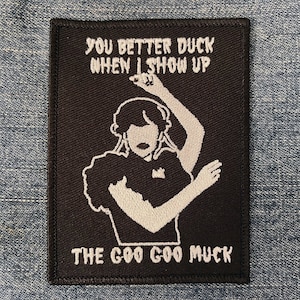 May include: Black and white embroidered patch with a woman dancing and the text "You better duck when I show up The Goo Goo Muck".