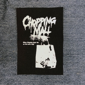 Può includere: Toppa termoadesiva in bianco e nero con il testo "Chopping Mall" e le parole "Where Shopping Costs You an Arm and a Leg!" La toppa presenta una borsa della spesa bianca con una mano e un braccio insanguinati al suo interno.