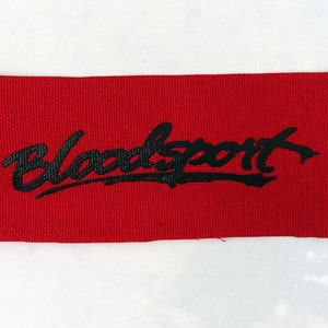 Puede incluir: Parche de tela rojo con texto bordado en negro que dice "Bloodsport".