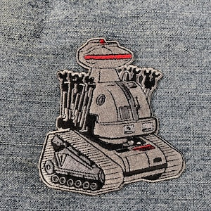 Può includere: Una toppa ricamata che rappresenta un robot con una luce rossa in cima, un corpo da carro armato e più braccia. La toppa è grigia e nera.