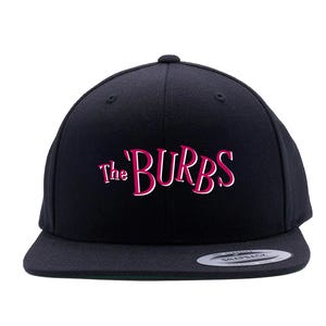 May include: Black snapback hat with the text "The Burbs" in a pink and white font. The hat has a flat brim and a structured crown. The hat is a classic style, suitable for casual wear.