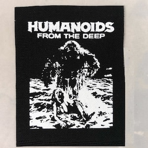 May include: Black and white embroidered patch with the text "Humanoids From The Deep" and a graphic of a creature emerging from the water.
