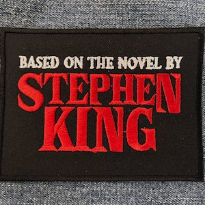 以下が含まれることがあります： 黒地に白文字で「Based on the novel by」と赤文字で「Stephen King」が刺繍されたパッチです。