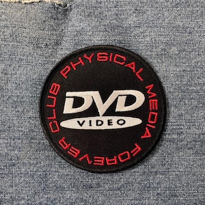 Pode incluir: Um remendo circular preto e vermelho com o texto "Physical Media Club Forever" em torno de um logotipo branco que diz "DVD Video".