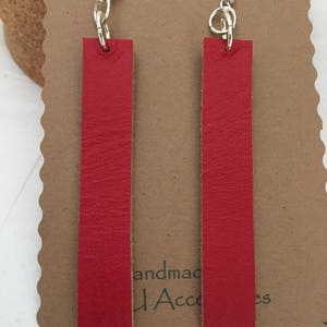 May include: A pair of red leather earrings with silver hooks. The earrings are rectangular in shape and have a smooth, polished finish.