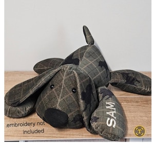 May include: A plush dog toy made of dark green fabric with a subtle plaid pattern and black silhouette prints. The toy features a black nose, two black eyes, and the name SAM embroidered in white on one ear. Text reads embroidery not included.