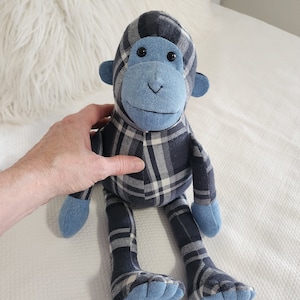 May include: A blue and white plaid monkey plush toy with a blue face and black eyes. The monkey is sitting on a white surface.