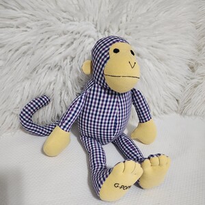 May include: A purple and white plaid monkey plush toy with yellow accents and a G-Pop label on the foot.