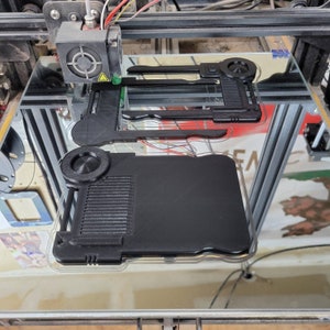 以下が含まれることがあります： 表面がテクスチャ加工され、丸いノブが付いた、3Dプリントされた黒いプラスチック製のオブジェクト。オブジェクトは3Dプリンターで印刷されています。