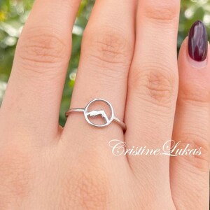 May include: A silver ring with a circle design featuring a mountain silhouette. The ring is on a hand with dark red nail polish.