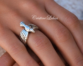 May include: A silver-toned ring featuring a detailed bird design. The bird is depicted in flight, with outstretched wings and a detailed feather pattern. The ring is a unique piece of jewelry with the text "Cristine Lukas".