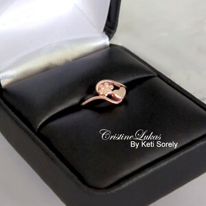 May include: Rose gold ring with a paw print and heart design. The ring is in a black ring box with the text "Cristine Lukas By Keti Sorely".