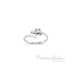K&ouml;nnte beinhalten: Ein silberner Ring mit einem Eidechsen-Design. Die Eidechse ist nach rechts gerichtet und hat einen eingerollten Schwanz. Der Ring ist offen und verstellbar.