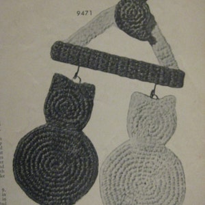 Pode incluir: Um móbile de crochê com três gatos pretos e brancos pendurados em uma moldura triangular. O móbile é feito de fio e tem um visual vintage.